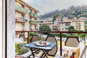 A balcony with a table set for two, overlooking a residential area with multiple buildings. - Casa Franca: Relaxing Como Stay with Mountain View (Como)