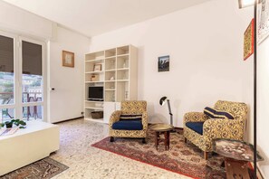 A living room with two patterned armchairs, a coffee table, a bookshelf, and a painting on the wall. - Casa Franca: Relaxing Como Stay with Mountain View (Como)