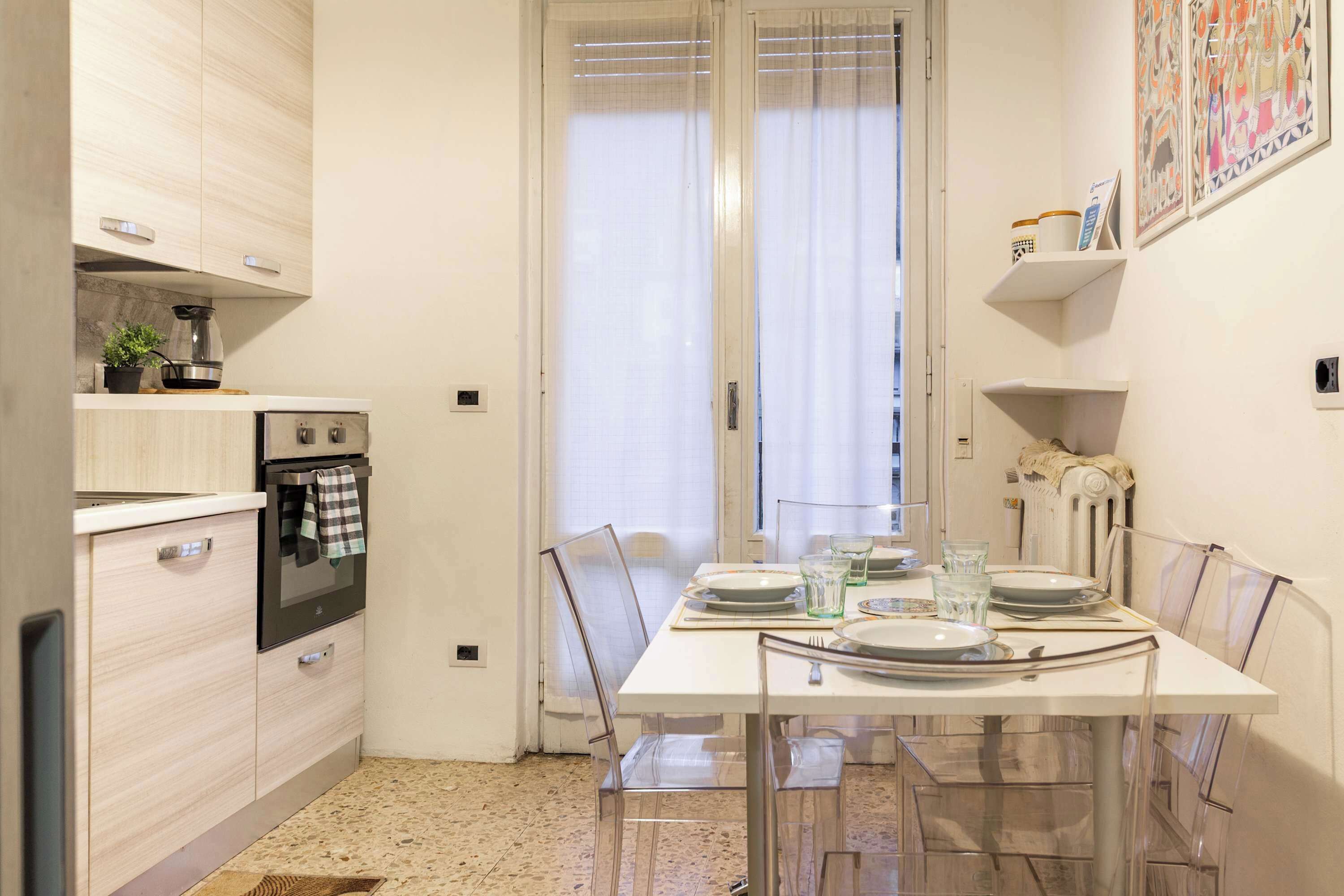 Una cucina compatta con elettrodomestici moderni, un tavolo da pranzo per quattro persone e una finestra con tende leggere.