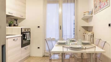 Una cucina compatta con elettrodomestici moderni, un tavolo da pranzo per quattro persone e una finestra con tende leggere.