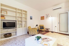A living room with a television, shelving, a patterned armchair, a coffee table, and a floor lamp. - Casa Franca: Relaxing Como Stay with Mountain View (Como)