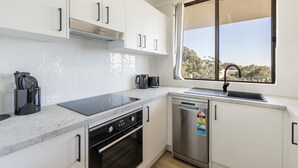 Een moderne keuken met witte kastjes, een ingebouwde oven, een vaatwasser en een raam met uitzicht op bomen.
