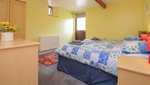 A bedroom with a bed, a bedside table, a radiator, a window, and a door. - The Old Wagon House (Torpoint)