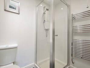 A glass-enclosed shower with a chrome showerhead and handheld shower attachment, a white toilet, and a chrome towel rack with multiple towel holders. - The Old Wagon House (Torpoint)