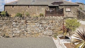 A stone building with a sloped roof, a small porch with a bench, and a sign indicating a restaurant. - The Old Wagon House (Torpoint)