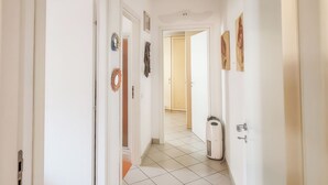 Un pasillo con paredes blancas, piso de baldosas y una puerta que da a otra habitación.