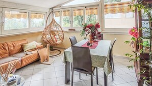 Una habitación acogedora con sofá, una silla colgante, una mesa de comedor con sillas y vistas amplias por las ventanas.