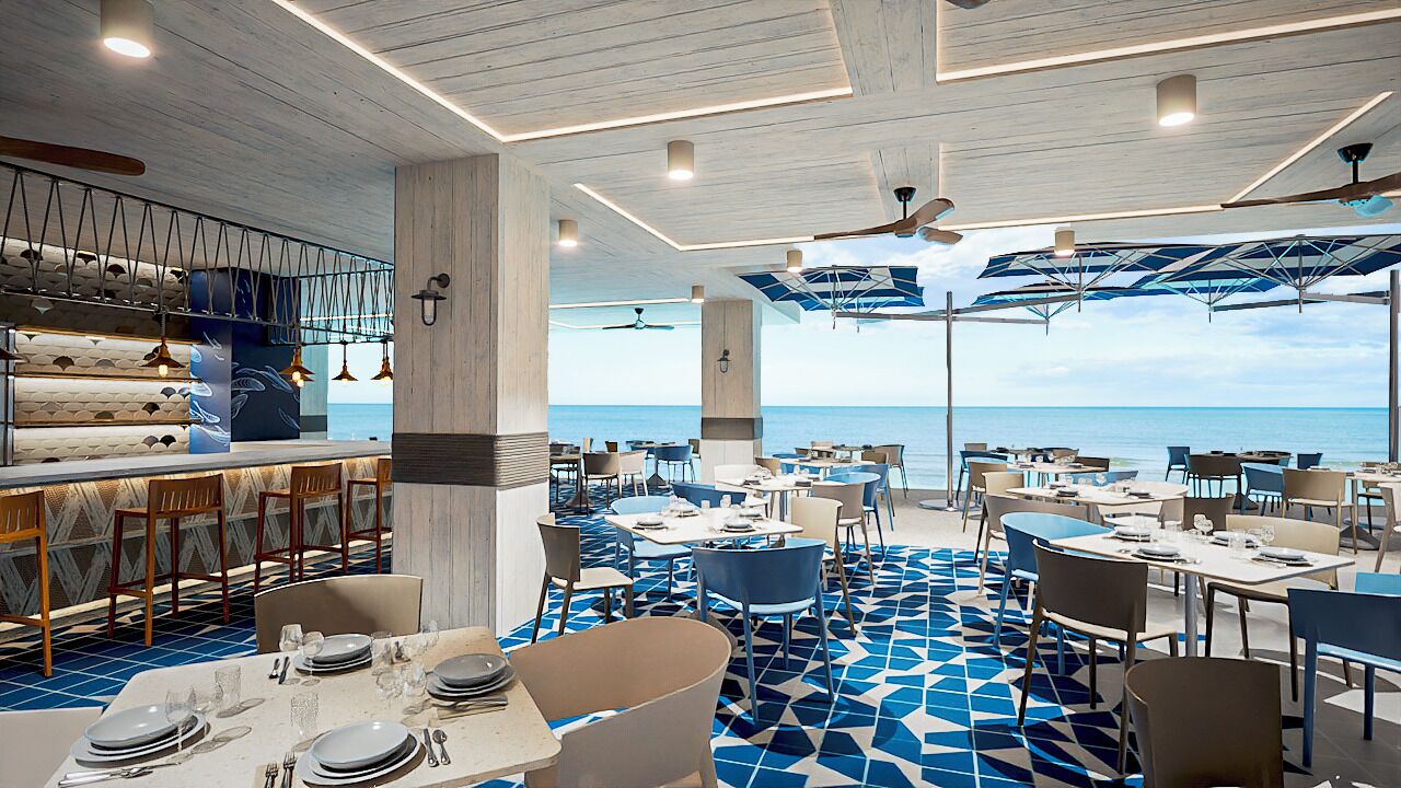 A restaurant with a view of the ocean, featuring a modern interior with blue and white geometric flooring, wooden tables and chairs, and a bar area with a unique ceiling design.