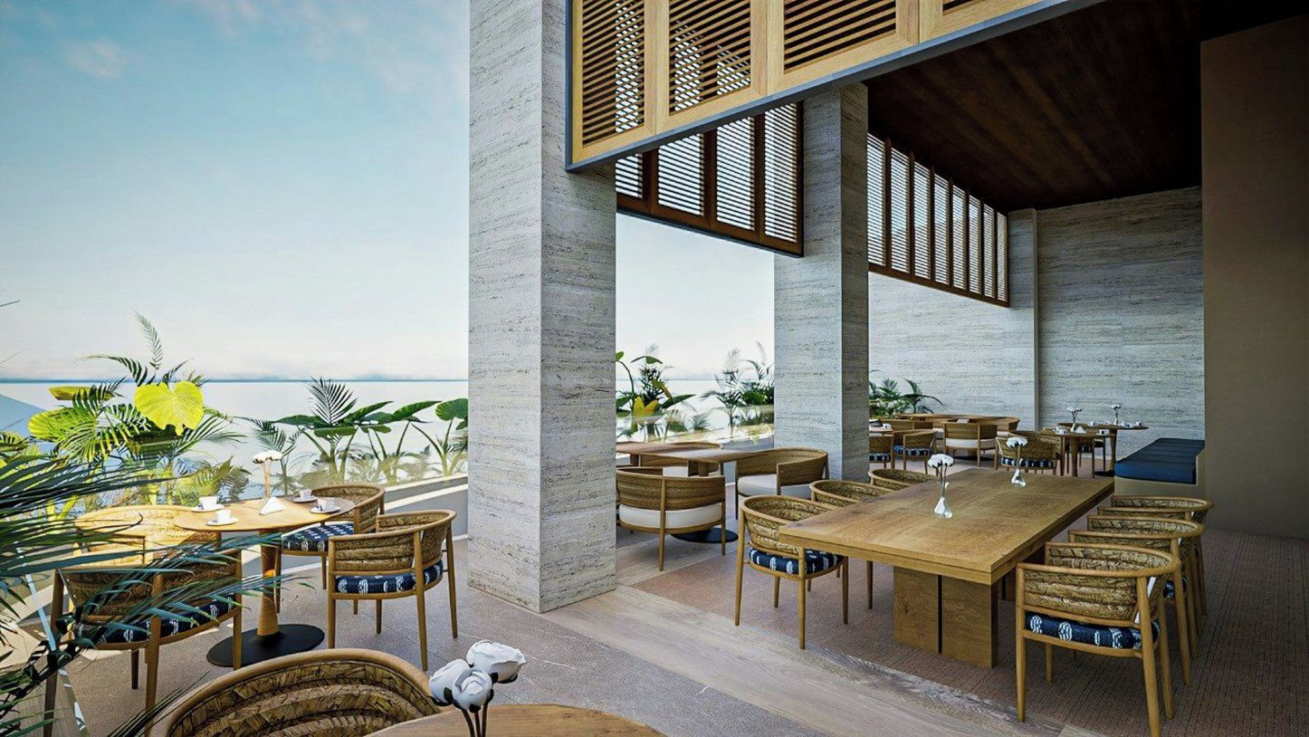 Un espace extérieur aménagé pour les repas, avec des tables et des chaises, une vue sur l’océan et des plantes tropicales.