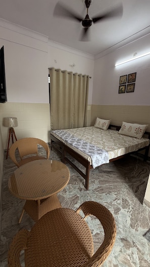 A room with a bed, two wicker chairs, a small table, a ceiling fan, and a lamp.