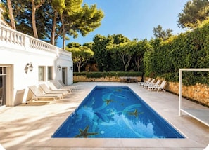 A rectangular swimming pool with a clear blue surface, surrounded by a white building with a balcony, and a stone wall with greenery. - Five-bedroom villa on Cap d'Antibes (Juan les Pins Antibes)