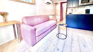 Et moderne opholdsrum med en lyserød sofa, et lille rundt bord, et træsidebord og et tekøkken med mikrobølgeovn.