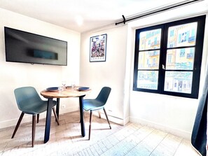 A room with a round table, two chairs, a flat-screen TV mounted on the wall, and a window with multiple panes. - Cocon Bonaparte 2 - Garibaldi (Nice)