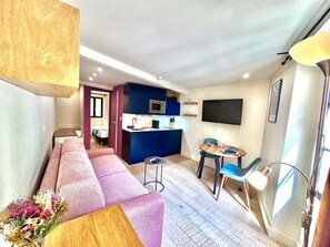 A compact living space with a sofa, a small kitchen area, a dining table, and a TV mounted on the wall. - Cocon Bonaparte 2 - Garibaldi (Nice)