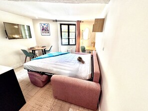 A small, compact room with a bed, a desk, a chair, and a window. - Cocon Bonaparte 2 - Garibaldi (Nice)