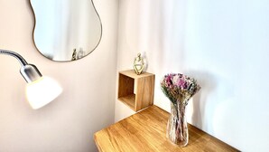 Et hjørne af et rum med et spejl på væggen, et skrivebord med en vase blomster og en lampe.