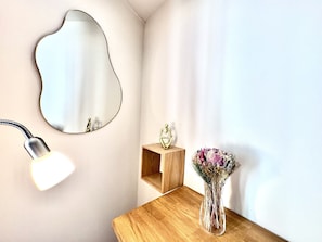 A corner of a room with a wall-mounted mirror, a desk with a vase of flowers, and a lamp. - Cocon Bonaparte 2 - Garibaldi (Nice)