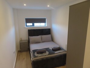 Ein kleines, modernes Schlafzimmer mit Bett, Nachttisch, Fenster und Kleiderschrank.