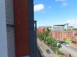 A residential street with parked cars, a row of houses, and a building with a modern design in the background. - Stylish 2 Bedroom Apartment in Liverpool City Centre (Liverpool)