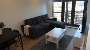 Una sala de estar moderna con un sofá negro, una mesa de centro blanca y una zona de comedor con una mesa y sillas negras.