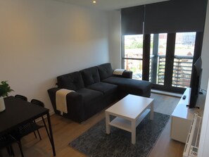 Ein modernes Wohnzimmer mit einer schwarzen Couch, einem weißen Couchtisch und einem Essbereich mit schwarzem Tisch und Stühlen.