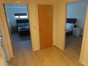 A hallway leading to a bedroom with a bed, a nightstand, and a window. - Stylish 2 Bedroom Apartment in Liverpool City Centre (Liverpool)
