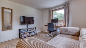 A modern living room with a flat-screen TV, a desk with a computer, a comfortable sofa, and a bookshelf with board games. - Chalet Elsa - renovated 4 bedroom chalet with a Jacuzzi & sauna in les Houches (Les Houches)