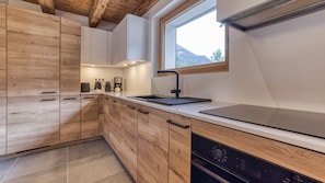 A modern kitchen with wooden cabinetry, a black countertop, and a window with a view of the outdoors. - Chalet Elsa - renovated 4 bedroom chalet with a Jacuzzi & sauna in les Houches (Les Houches)