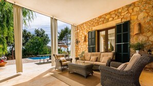 A covered outdoor seating area with wicker furniture, a stone wall, and a view of a pool. - Son Polvell, Finca 5StarsHome Mallorca (Andratx)