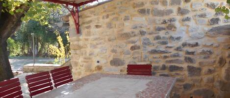 An outdoor seating area with stone walls, a tiled floor, and wooden benches.