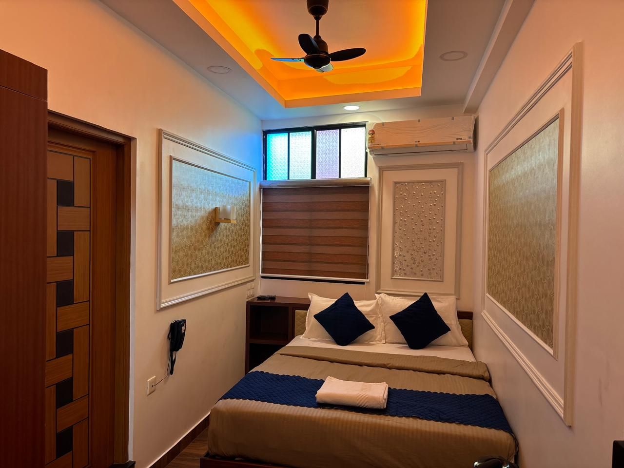 Una camera d'albergo con un letto, una ventola a soffitto, una finestra con tende e opere d'arte alle pareti.