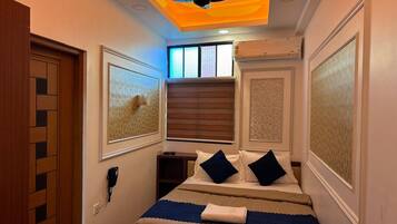 Una camera d'albergo con un letto, una ventola a soffitto, una finestra con tende e opere d'arte alle pareti.