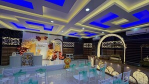 A banquet hall with tiered seating, a stage with floral decorations, and a modern ceiling design. - Odyssey Rendezvous (Kunnathunad)
