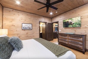 Een slaapkamer met een bed, een dressoir, een plafondventilator en een televisie aan de muur.