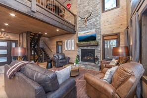 A spacious living room with leather sofas, a fireplace, and a stone accent wall. - ChambPlace: Pool, HotTub, Wifi, Theater, Games, EVCharger, OutdoorFireplace (Sevierville)