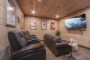 A room with wooden walls, a large flat-screen TV, leather seating, and framed movie posters. - ChambPlace: Pool, HotTub, Wifi, Theater, Games, EVCharger, OutdoorFireplace (Sevierville)