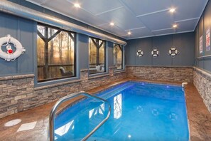 An indoor swimming pool with stone walls and large windows. - ChambPlace: Pool, HotTub, Wifi, Theater, Games, EVCharger, OutdoorFireplace (Sevierville)