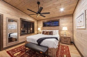 Ein Schlafzimmer mit Holzwänden, einem Bett, Nachttischlampen, einem Deckenventilator und einem Spiegel.