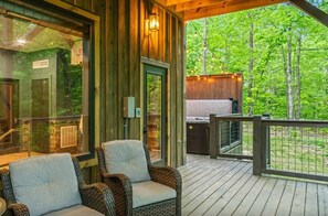 A wooden deck with wicker chairs, a glass door leading to a room, and a view of a forest. - ChambPlace: Pool, HotTub, Wifi, Theater, Games, EVCharger, OutdoorFireplace (Sevierville)