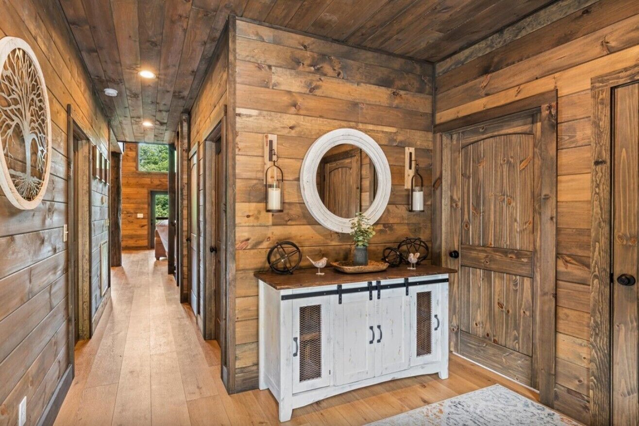 Un couloir aux murs en bois, un meuble blanc aux portes vitrées et un miroir rond placé au-dessus.