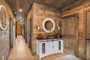 A hallway with wooden walls, a white cabinet with glass doors, and a round mirror above it. - UndHrvstMoon: Pool, HotTub, Wifi, Theater, Games, Pets, OutdoorFireplace (Sevierville)