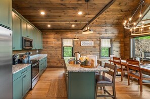 A kitchen with wooden walls, a central island, and a dining area with wooden chairs. - UndHrvstMoon: Pool, HotTub, Wifi, Theater, Games, Pets, OutdoorFireplace (Sevierville)