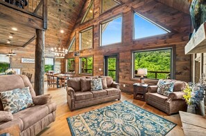 A spacious living area with a high ceiling, large windows, and a view of the outdoors. - UndHrvstMoon: Pool, HotTub, Wifi, Theater, Games, Pets, OutdoorFireplace (Sevierville)