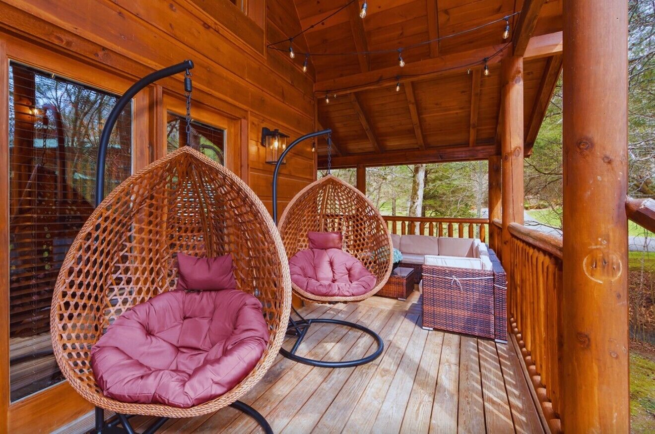 A wooden deck with two wicker hanging chairs and a sofa.