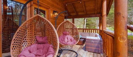 A wooden deck with two wicker hanging chairs and a sofa.