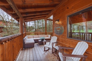 A wooden deck with a sofa, chairs, and a table. - PeacefulCreek: Pool, HotTub, Wifi, FirePit, Pets, Creek, Resort Facilities (Sevierville)