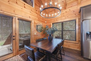 Ein Holzinterieur mit einem Esstisch, Stühlen, einer Chandelieber und einem Kühlschrank.