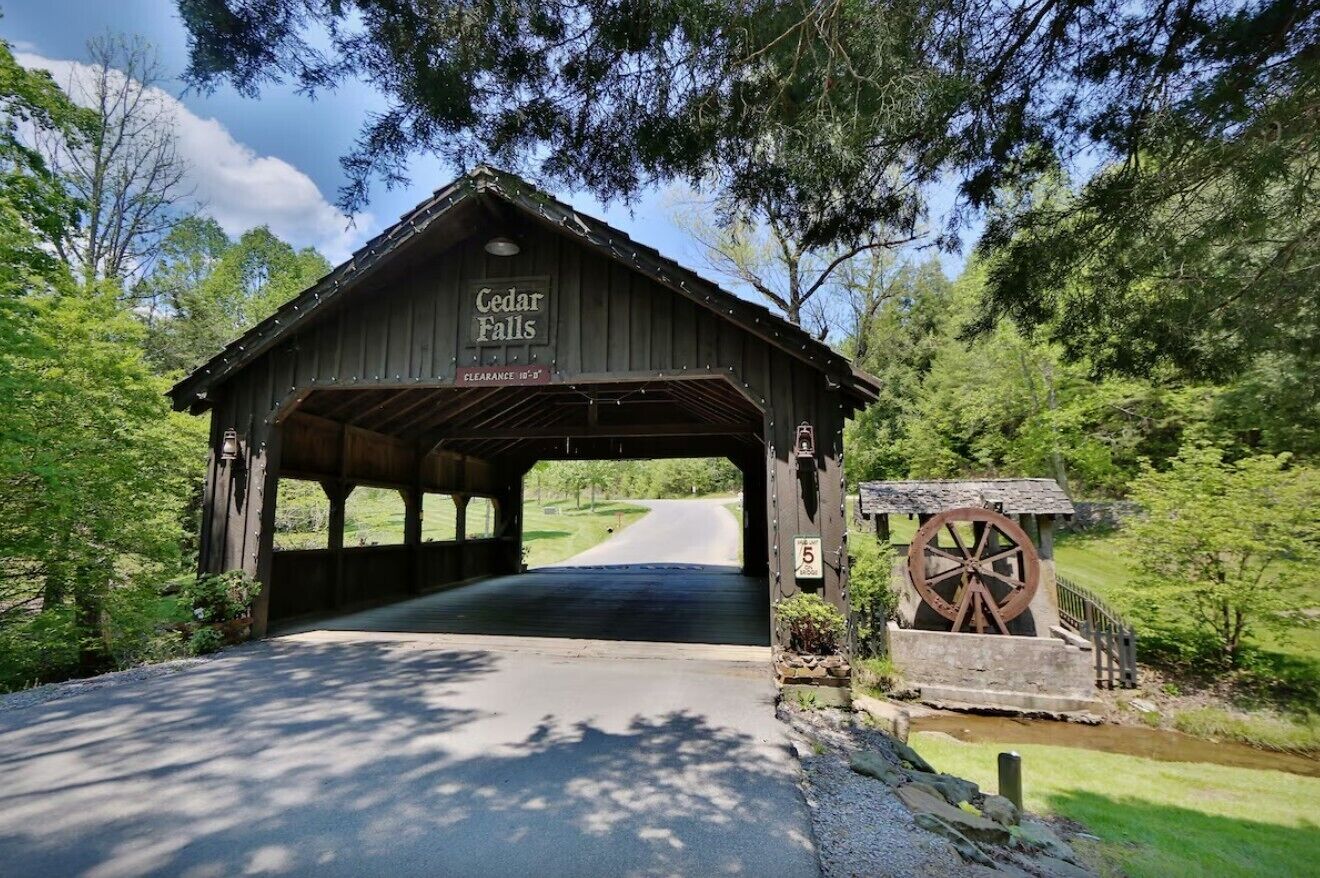A wooden covered bridge with a sign reading 'Cedar Falls' and a water wheel to the right.