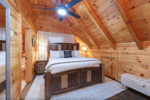A wooden cabin bedroom with a bed, bedside tables, a bench, and a ceiling fan. - PeacefulCreek: Pool, HotTub, Wifi, FirePit, Pets, Creek, Resort Facilities (Sevierville)