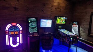 Et værelse med trævægge, en neon jukebox, en digital jukebox, en videospilskonsol og en tøndelok.